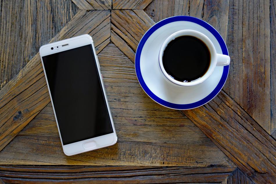 smartphone and white cup with coffee on a wooden table