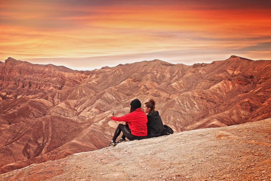 People, sitting on the beautiful and colorful mountains, at colorful sunset in the desert of Death Valley in California, USA