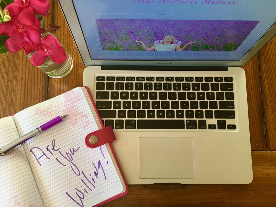 Laptop with the colorful screen, notebook with the pen and purple flowers in the vase, on the table