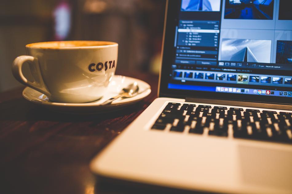 White Macbook and beautiful, white cup of coffee on the plate with spoon on the table