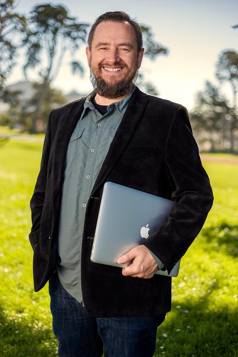 Portrait of the smiling, bearded man, in the suit, with the Mackbook, on the colorful and beautiful meadow