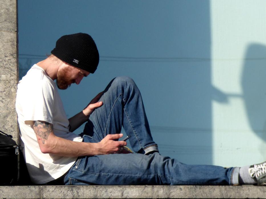 Man in black hat, reading on the smartphone, in shadow and light, outdoors