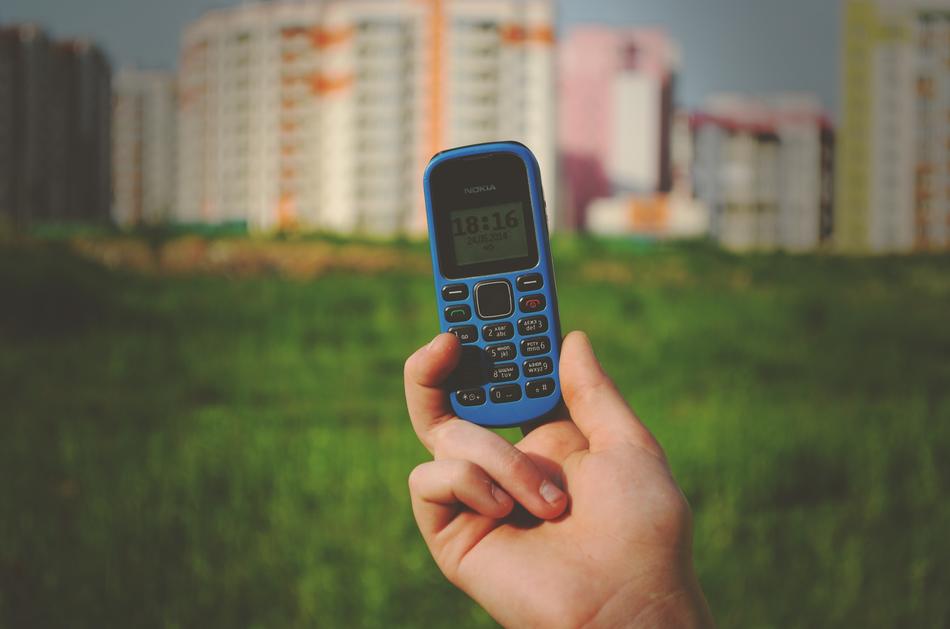 Holding blue Nokia phone in the hand at background with green grass and colorful buildings