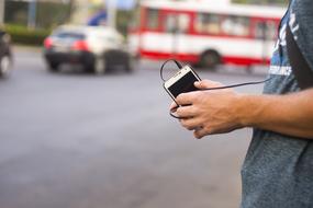 Guy, holding smartphone in the hand, white listening to music, on the street