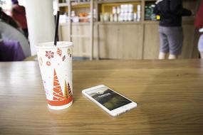 smartphone and a drink in a paper cup on a table in a cafe