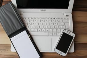 Top view with the white notebook, laptop and smartphone, on the wooden table