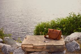 red bag and smartphone lie on wooden boards near the river