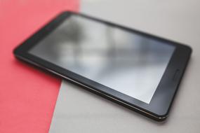 Close-up of the shiny, black tablet on the red and grey surface