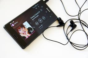 Black "Sony Xperia Z3" smartphone with earphones, with music on play