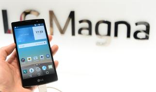 Person holding black "LG Magna" smartphone in hand, near the wall with "LG Magna" sign