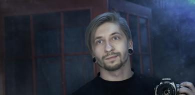 handsome caucasian man holds photo camera at dark foggy background