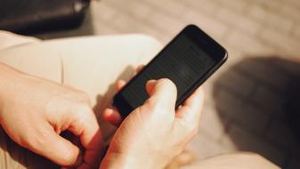 Person, holding shiny, black Iphone in the hand, in sunlight