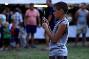 Kid boy taking photo on smartphone, near the other people in the park