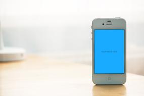 Standing, white Iphone, with blue screen, with the shadow on the wooden table, in light