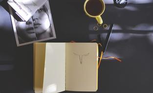 Notebook with Sketch, photo and coffee on black desk