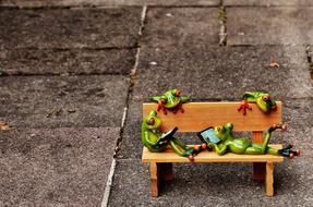 Cute and colorful figures of the frogs on the wooden bench, on the ground