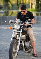 Guy with sunglasses on the shiny motorbike, near the colorful plants