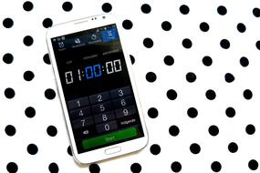 White smartphone with timer, on the white surface with black dots, clipart