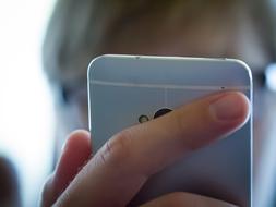 Person with glasses, holding turquoise smartphone in the hand