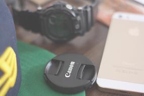 Close-up of the black and white "Canon" camera cap near the black watch and beautiful, gold and white Iphone