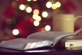 open bible and cup of hot chocolate on christmas lights background