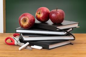 burgundy apples on a stack of black notebooks and scissors on a table