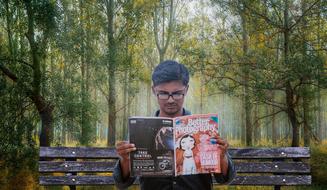 young man reads a magazine on a park bench