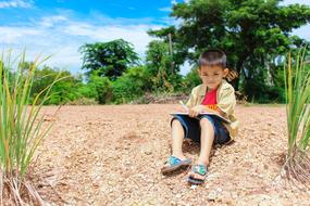 boy reads a book by the pond