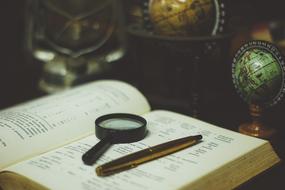 magnifier and pen lie on an open book