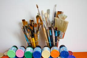 brushes in glasses and paints on a table against a white wall