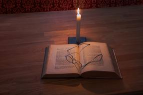 Glasses on open book and burning candle