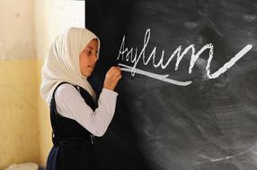 girl is writing asylum on a blackboard