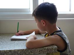 a boy writes with pencil on the notebook at a table in China