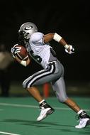 photo of a running american football player with a ball in gray-white uniform