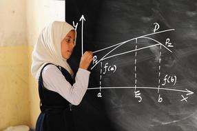 muslim girl drawing mathematics curve with chalk on blackboard