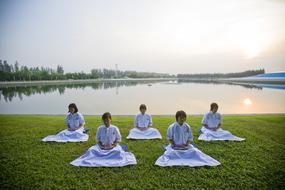 Meditation at sunrise, five asian Girls sitting on grass at water