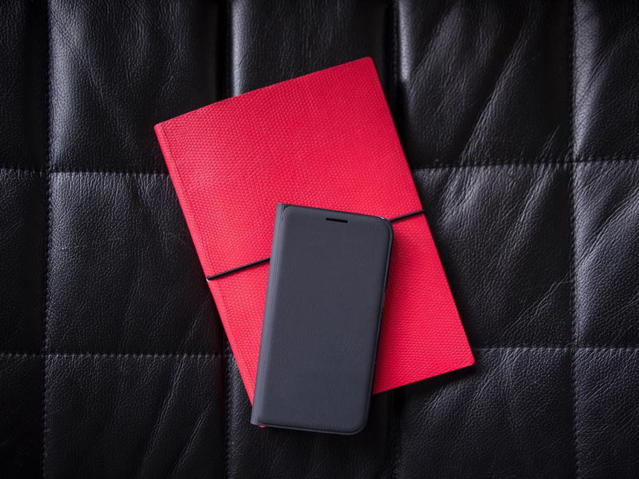 Close-up of the black, leather smartphone on the red notebook, on the black surface