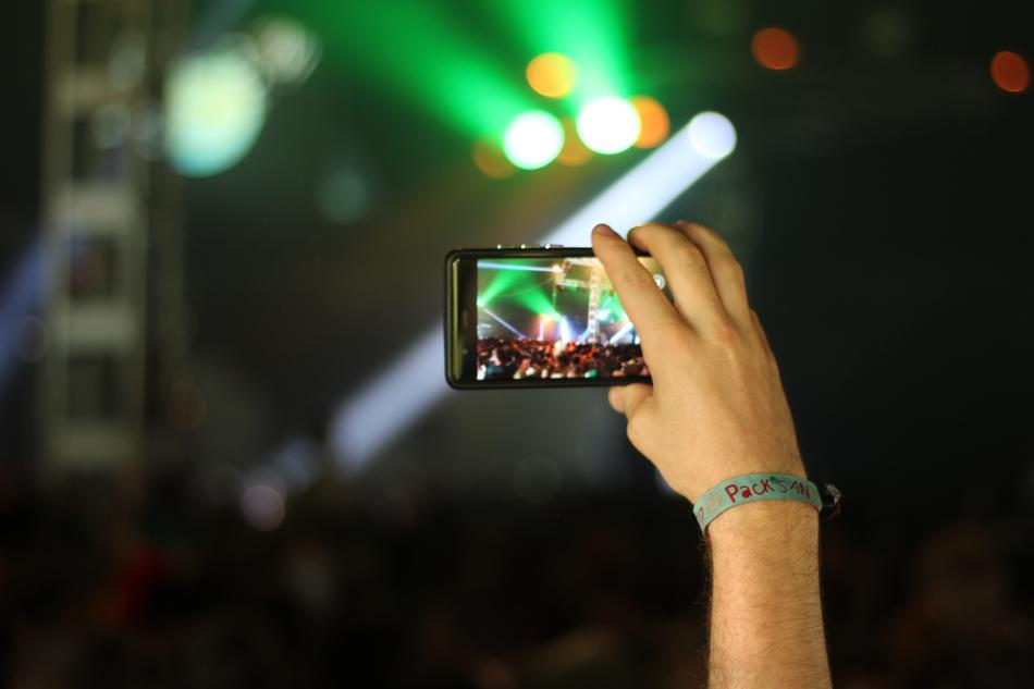 man filming concert on smartphone with blurred background