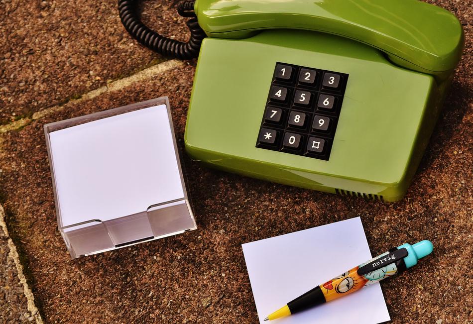 Close-up of the green, black and white, retro phone near the notes and colorful pen