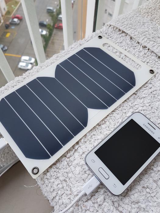 Close-up of the white 'Samsung' smartphone on the charge, near the solar panel, in Brazil