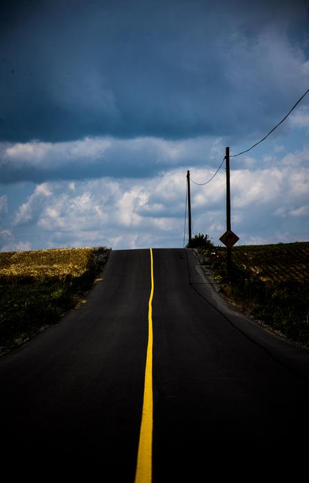 Landscape with the road with yellow line, among the colorful fields, under the clouds