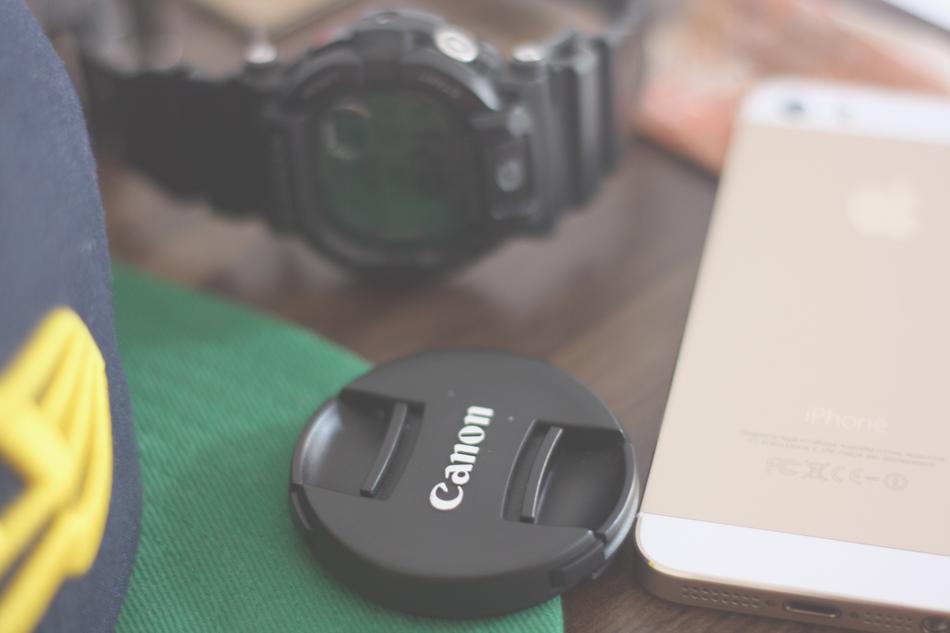 Close-up of the black and white 'Canon' camera cap near the black watch and beautiful, gold and white Iphone