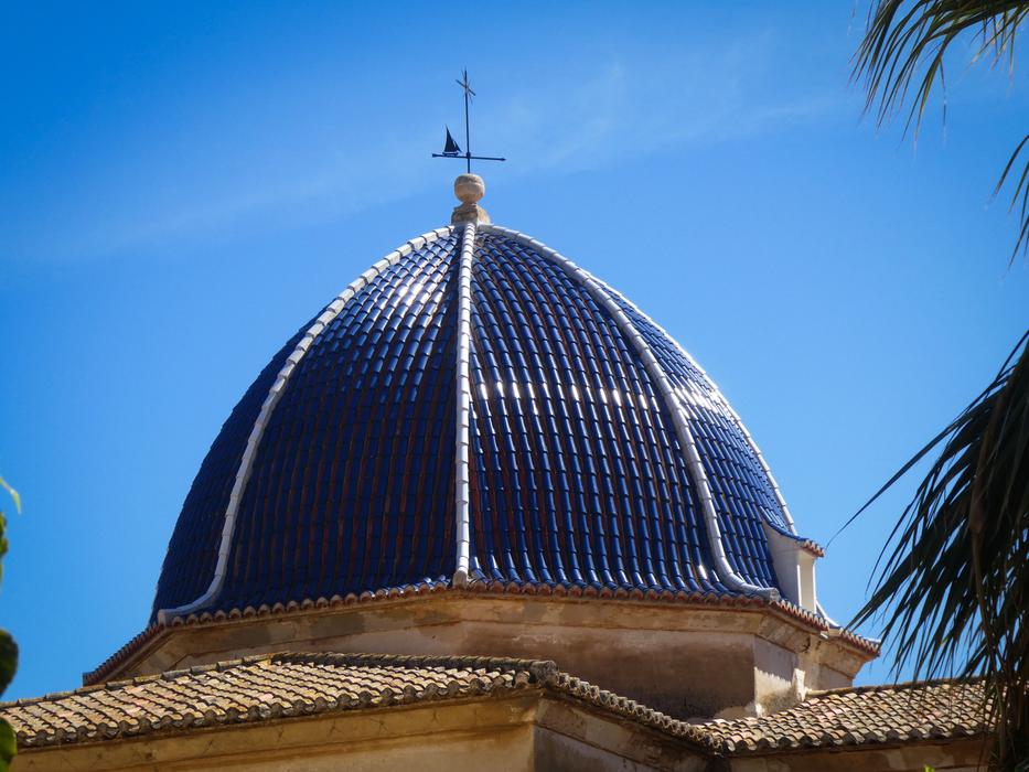 Shiny dome of the church, near the tree, in Denia, Spain, under the blue sky