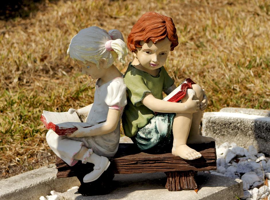 sculpture of a boy and a girl with books on a bench