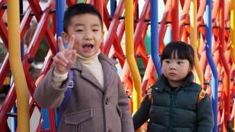 Cute brother and sister, showing peace sign, near the colorful fence