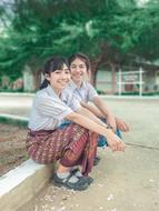 Beautiful, smiling girl students, sitting near the school in Thailand