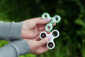 Girl, holding colorful, glossy fidget spinners in the hands, at background with the green plants