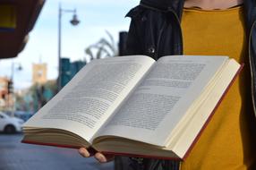 Person, open book, on the street, under the blue sky with clouds