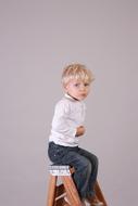 the boy sits neatly on a wooden chair