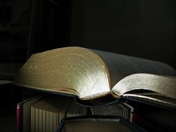 Open book on the other books, in light and shadow, at dark background